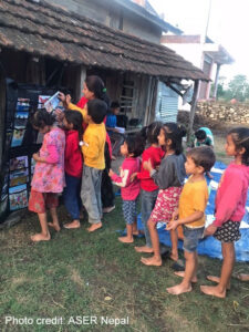  A group of children queue up with their volunteer teacher to look at leaflets as part of the My Village project, Nepal.