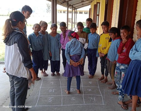 A group of girls and boys play a game on the floor where they jump on a number and then discuss an issue, Nepal.