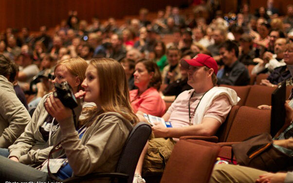 A crowd of academic conference participants sit in a lecture theatre.