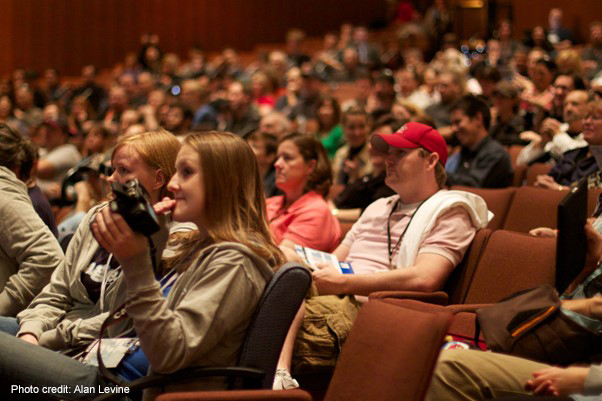 A crowd of academic conference participants sit in a lecture theatre.