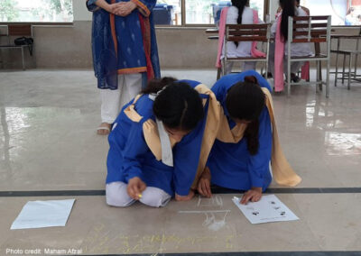 Two female students kneel on the floor and write with chalk during a Thinking Routine activity.