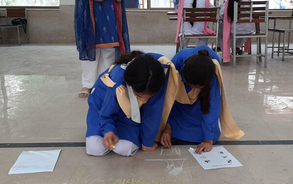 Two female students kneel on the floor and write with chalk during a Thinking Routine activity.