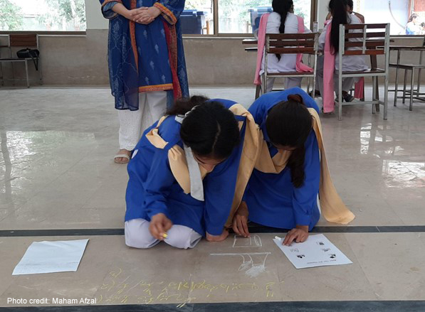 Two female students kneel on the floor and write with chalk during a Thinking Routine activity.