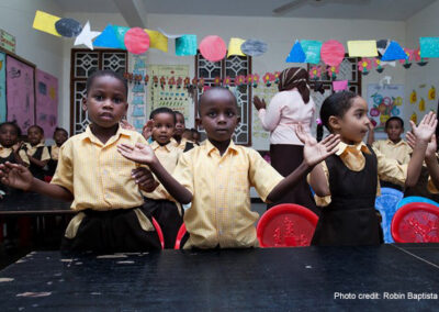 Early childhood education workshop school visit, Zanzibar. 3 children in the foreground with hands spread perhaps to clap