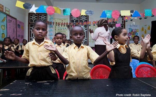 Early childhood education workshop school visit, Zanzibar. 3 children in the foreground with hands spread perhaps to clap