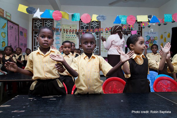 Early childhood education workshop school visit, Zanzibar. 3 children in the foreground with hands spread perhaps to clap