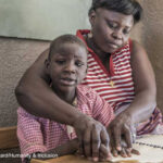 A boy receives help to read from a female teacher through an inclusive education project, Uganda.