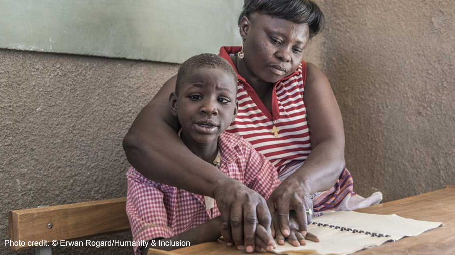 A boy receives help to read from a female teacher through an inclusive education project, Uganda.