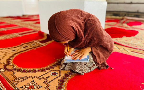 Afghan girl does her school work sitting on a carpet in a class run by Street Child Afghanistan.
