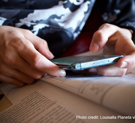 A student refers to their mobile phone alongside their textbook in class.
