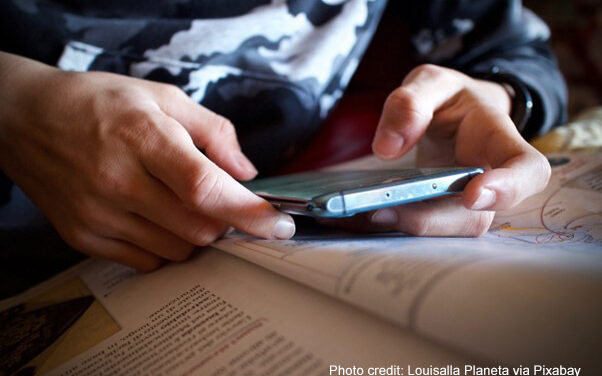 A student refers to their mobile phone alongside their textbook in class.