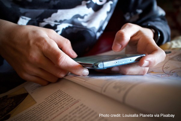 A student refers to their mobile phone alongside their textbook in class.