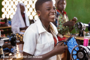 smiling girl sitting at sewing machine in class