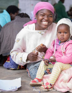 Smiling learner with baby in a community-based accelerated learning centre