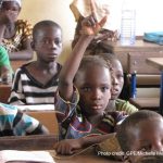 A girl in the classroom in Mali raises her hand to answer a question from the teacher.