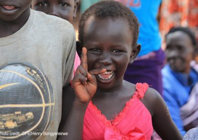 Young girl in a bright pink dress smiling at Kiryandongo refugee settlement, Uganda.