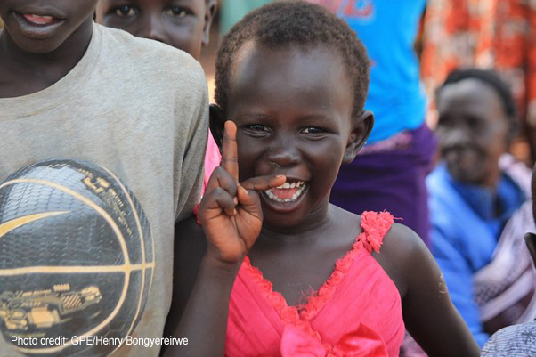 Young girl in a bright pink dress smiling at Kiryandongo refugee settlement, Uganda.