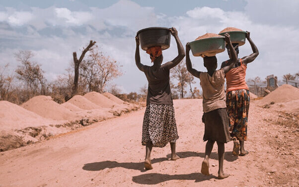 Two women and a girl carrying basins on their heads, while walking barefoot, Uganda.