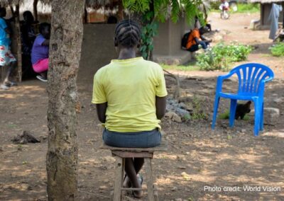 Adolescent girl in yellow t shirt sits alone outside a classroom, Uganda