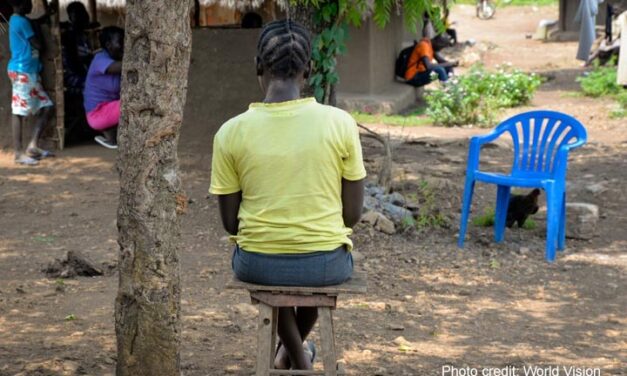 Adolescent girl in yellow t shirt sits alone outside a classroom, Uganda