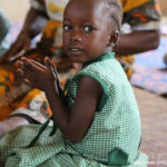 A young girl wearing green uniform, clapping in pre-primary school, Sierra Leone.