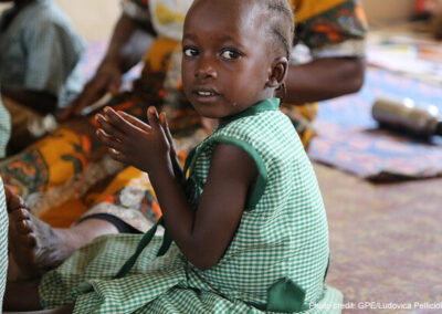 A young girl wearing green uniform, clapping in pre-primary school, Sierra Leone.