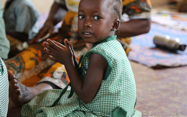 A young girl wearing green uniform, clapping in pre-primary school, Sierra Leone.