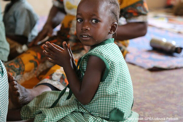 A young girl wearing green uniform, clapping in pre-primary school, Sierra Leone.