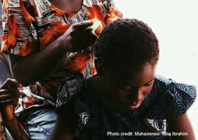 Girl looks down as she has her hair combed from behind.