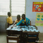 Three young students play with ordering the alphabet in a classroom, rural Ghana.