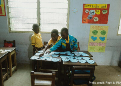 Three young students play with ordering the alphabet in a classroom, rural Ghana.