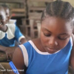 Girl dressed in blue writes in classroom.