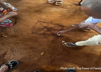 Parents draw on the ground while playing a traditional game.