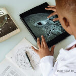 Boy learns about planets on his tablet and with a book.