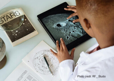 Boy learns about planets on his tablet and with a book.