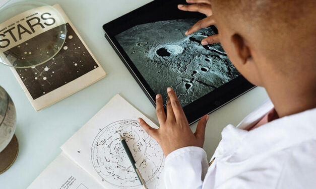 Boy learns about planets on his tablet and with a book.