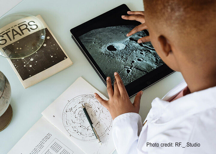 Boy learns about planets on his tablet and with a book.