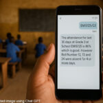 A teacher’s hand holds a mobile phone telling them about the attendance record of their class for the last 30 days.