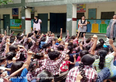 Teachers stand at the front of an outdoor class of primary students, India