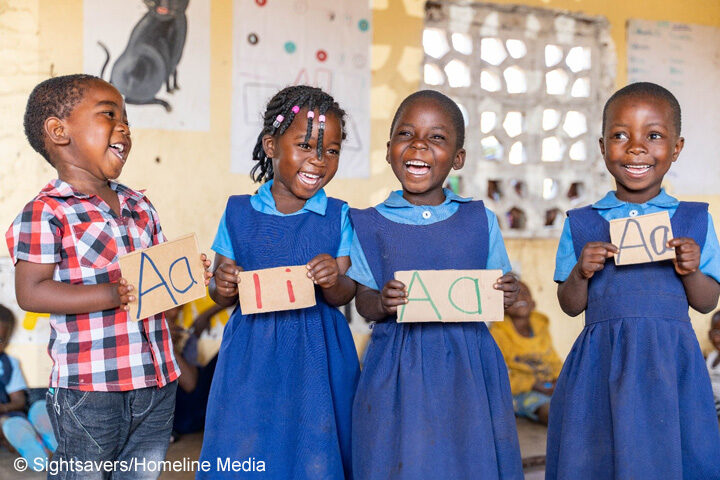 Three primary children holding up letter cards and smiling