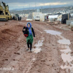 Muslim girl in headscarf walking on muddy ground in settlement, Idlib, Syria