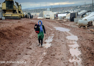 Muslim girl in headscarf walking on muddy ground in settlement, Idlib, Syria