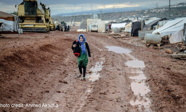 Muslim girl in headscarf walking on muddy ground in settlement, Idlib, Syria