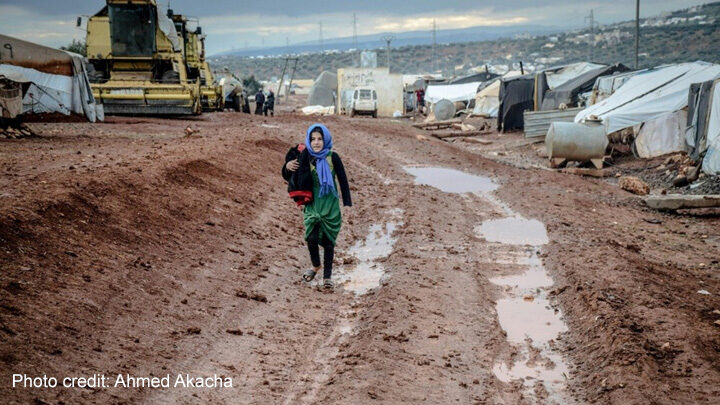 Muslim girl in headscarf walking on muddy ground in settlement, Idlib, Syria