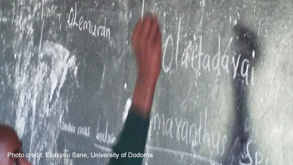 An arm reaches up to write on the blackboard.