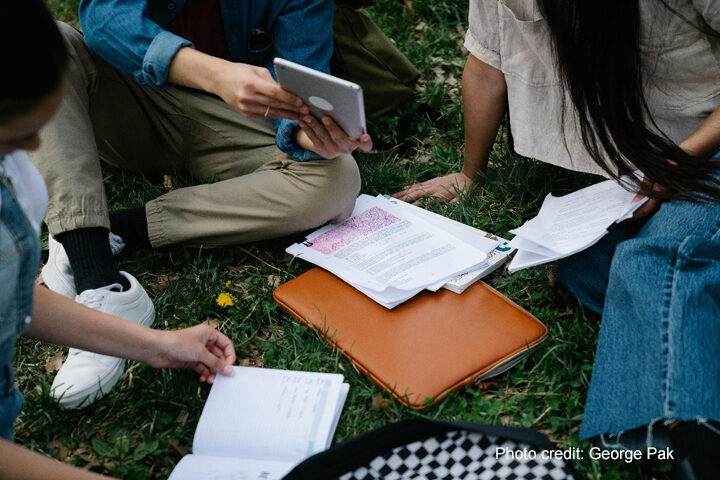 Group of university students study together sitting on the ground.