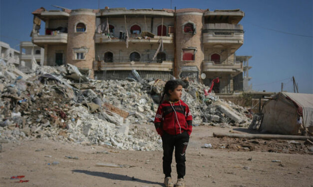 Girl stands in front of ruined buildings