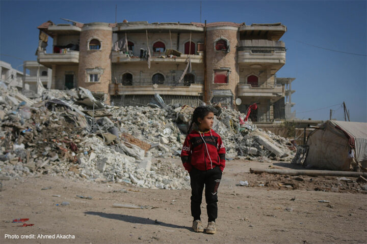 Girl stands in front of ruined buildings
