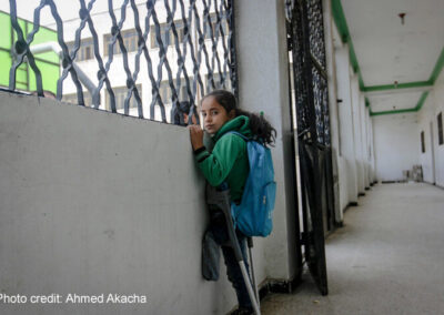 Girl refugee with amputated leg and crutches looks out of the window of a school in a refugee camp, Idlib, Syria.