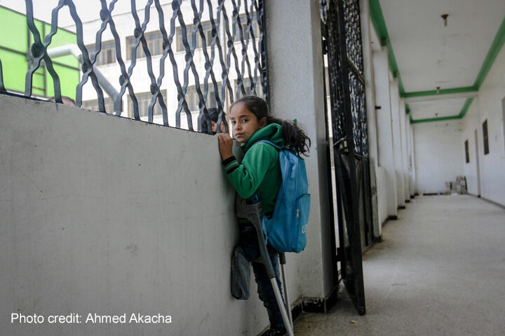 Girl refugee with amputated leg and crutches looks out of the window of a school in a refugee camp, Idlib, Syria.